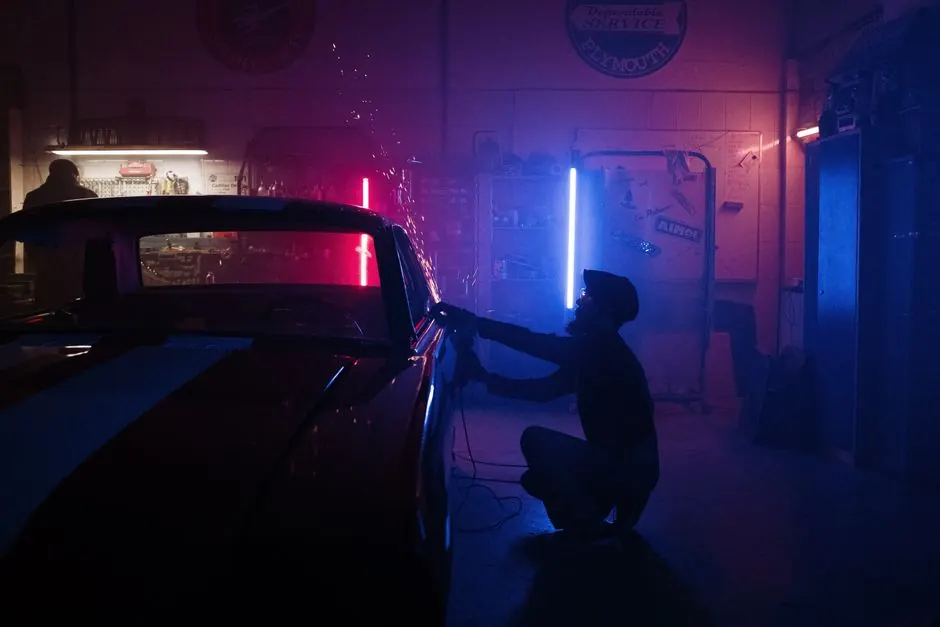 A mechanic works on a car in a neon-lit garage, creating a vibrant, moody atmosphere.